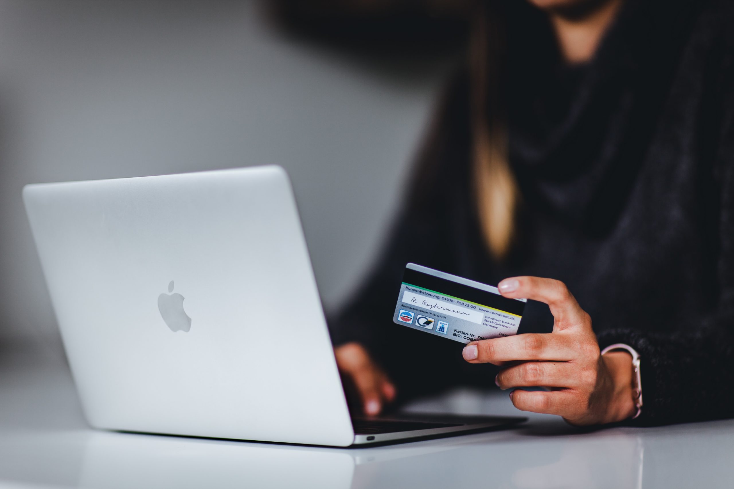 A woman facing an open laptop holding a credit card.