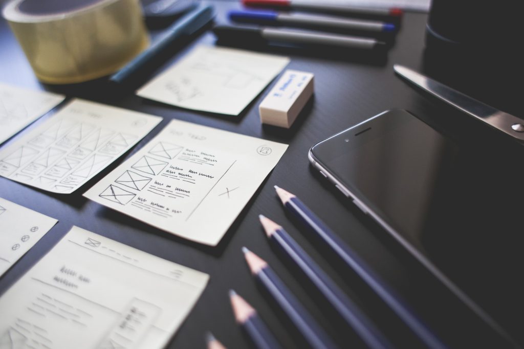 Sketches of UX design with pencils and a smart phone laid out on a black table