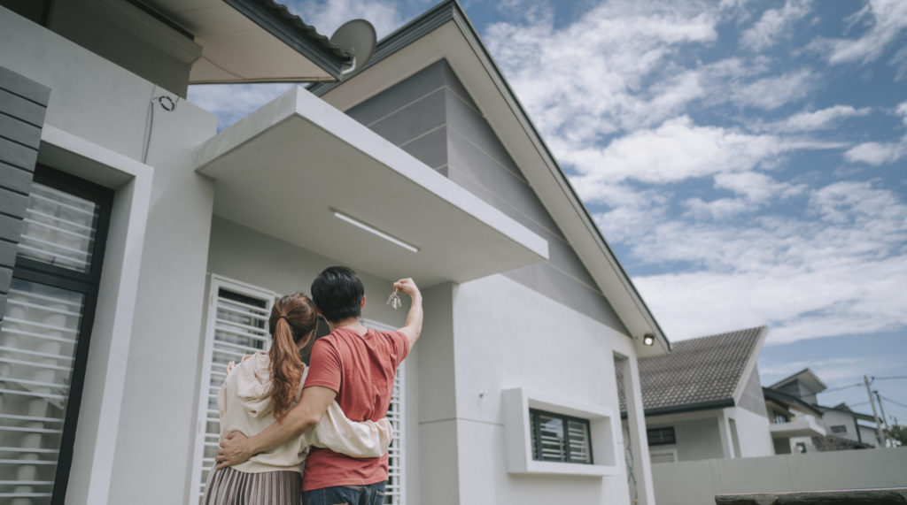 Couple standing in front of new house holding up keys.
